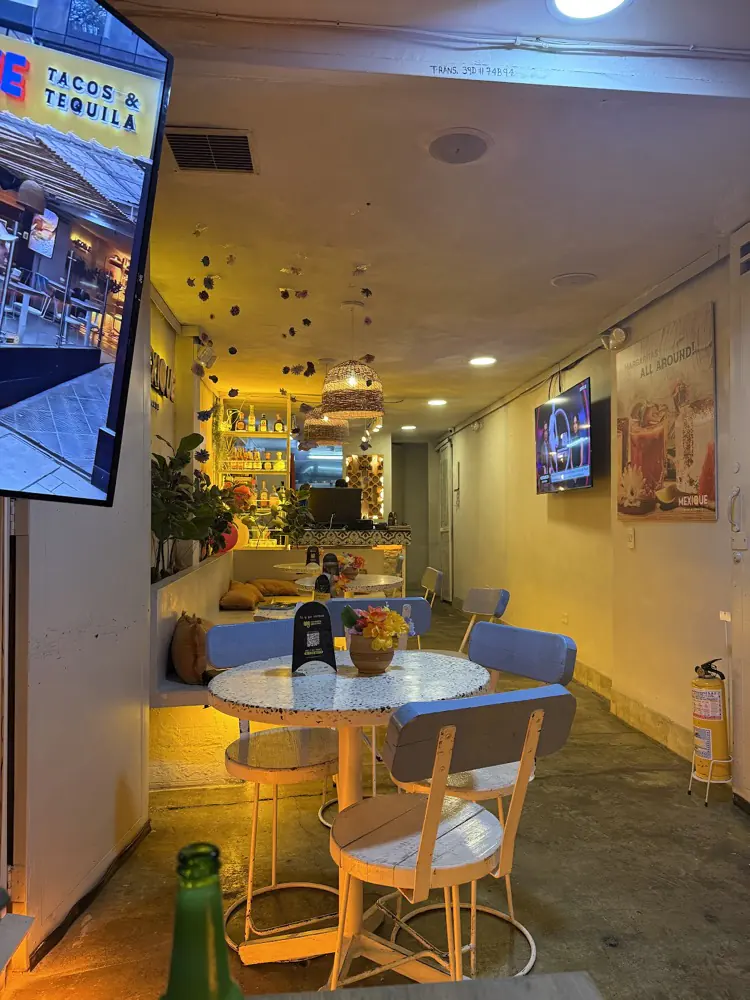 Interior de Mexique con mesas de terrazo, sillas azules y luces cálidas